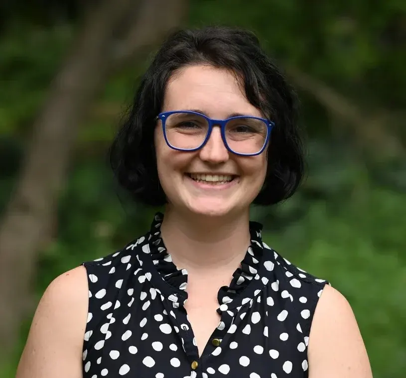 Woman standing with glasses with wooded background blurred